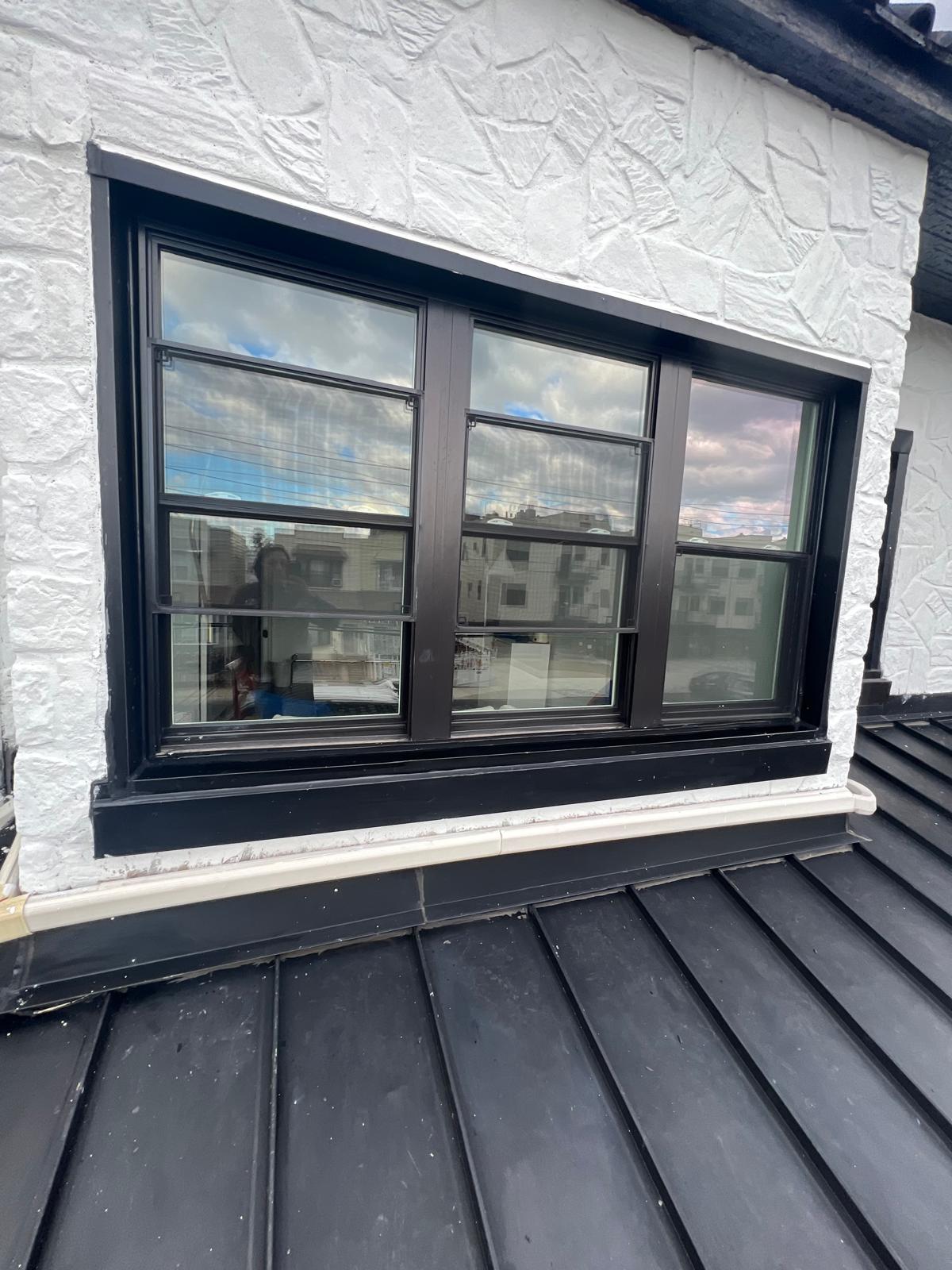 Finished charcoal-gray standing-seam metal roof at a window and sidewall transition