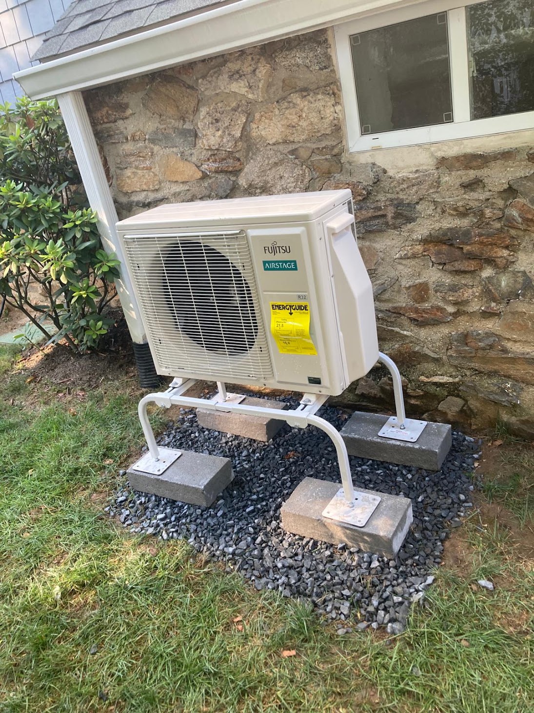 Outdoor heat-pump condenser beside a stone foundation at a Kellets project