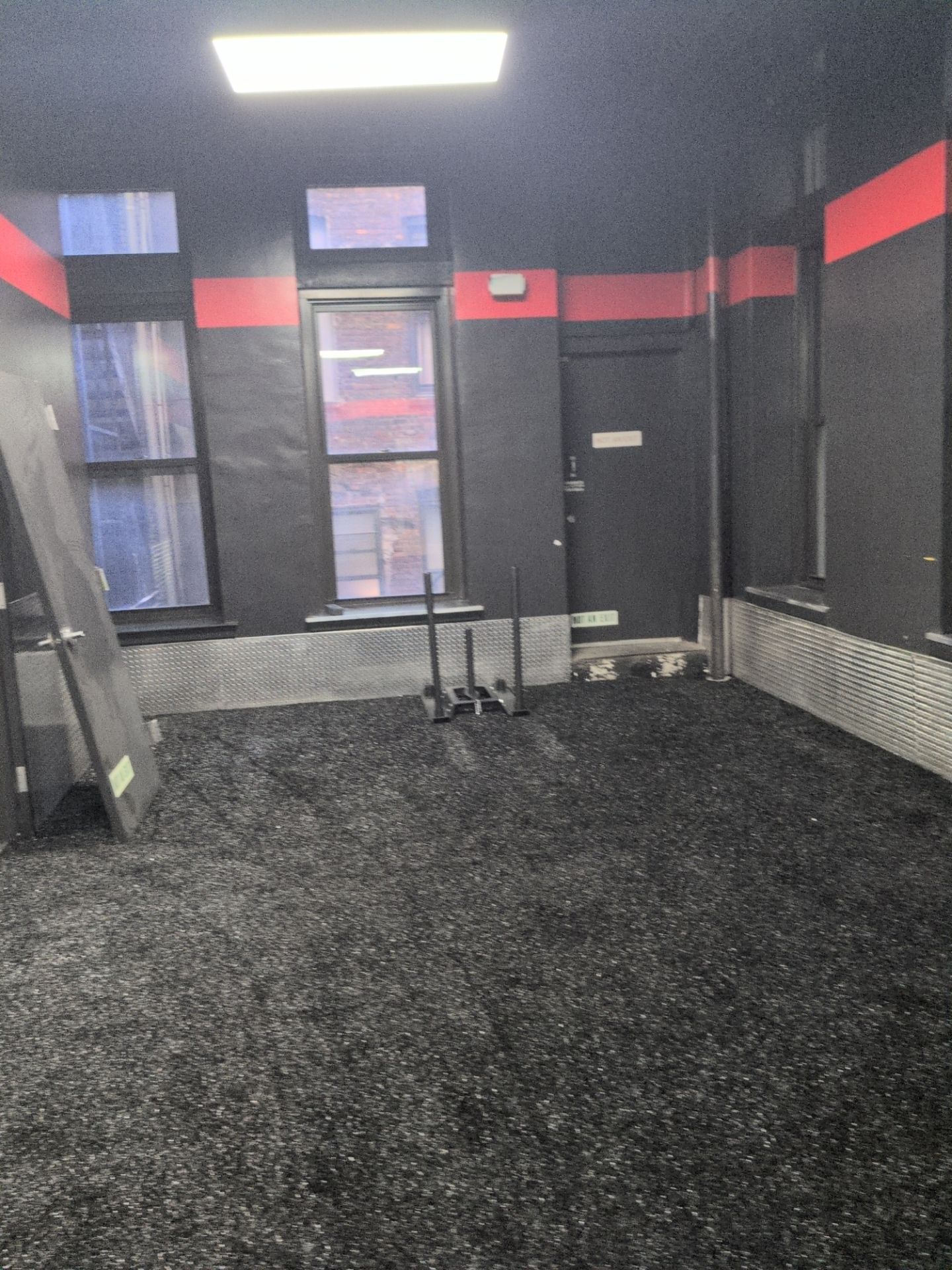 Black and red fitness room with rubber flooring and diamond-plate wall protection documented by Kellets