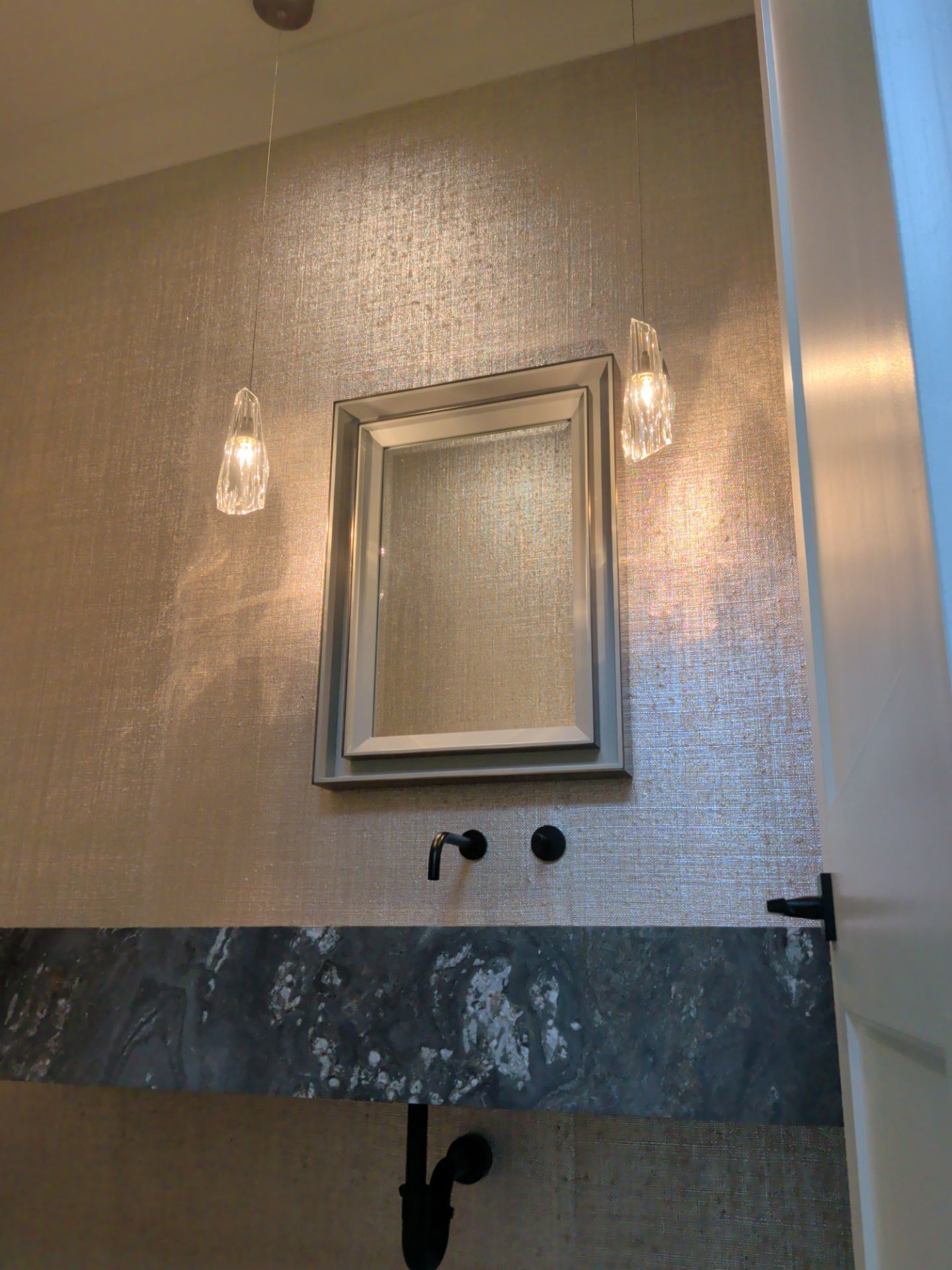 Close detail of textured wallcovering aligned around a mirror, sconces and stone vanity