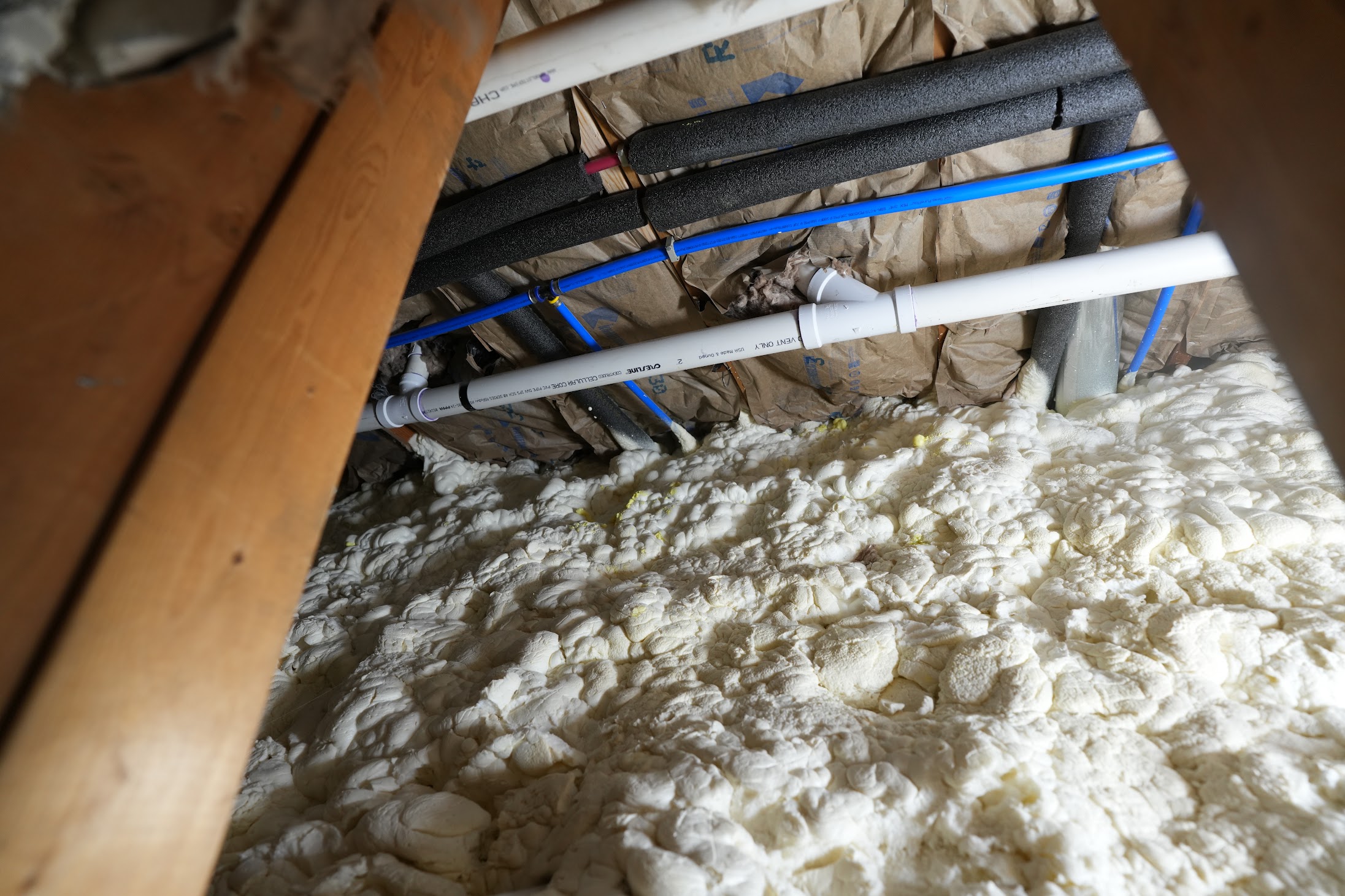 Spray foam insulation coordinated around plumbing and insulated piping in a Kellets project